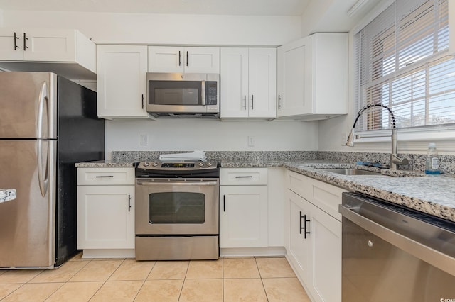 kitchen featuring appliances with stainless steel finishes, light tile patterned floors, white cabinets, sink, and light stone counters