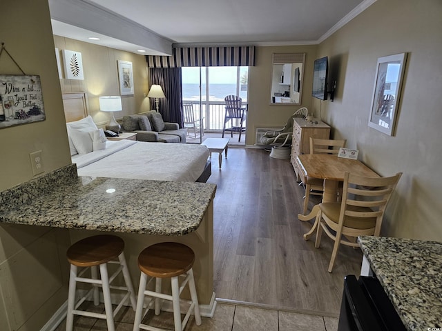 kitchen featuring hardwood / wood-style flooring, a kitchen bar, light stone countertops, and ornamental molding