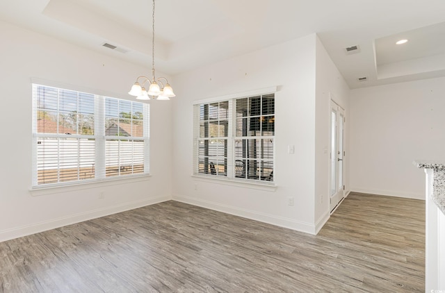 unfurnished room featuring an inviting chandelier, wood-type flooring, and a tray ceiling