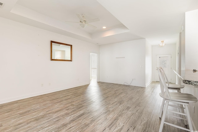 unfurnished living room with ceiling fan, a tray ceiling, and light hardwood / wood-style flooring