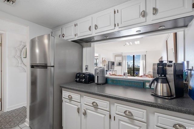 kitchen featuring tile patterned floors, stainless steel fridge, white cabinets, and a textured ceiling