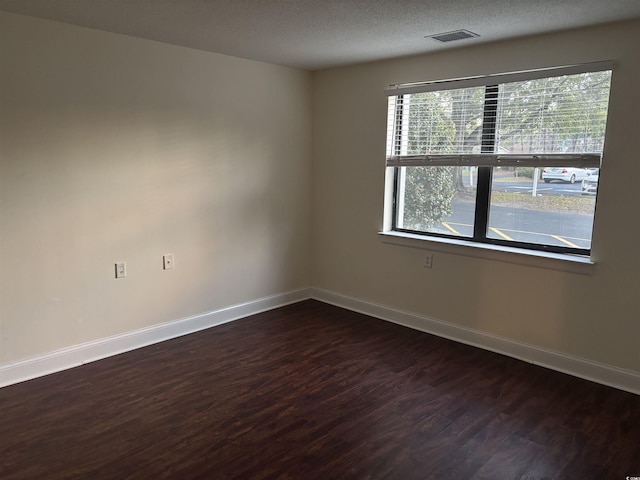 empty room featuring visible vents, a textured ceiling, baseboards, and dark wood-type flooring