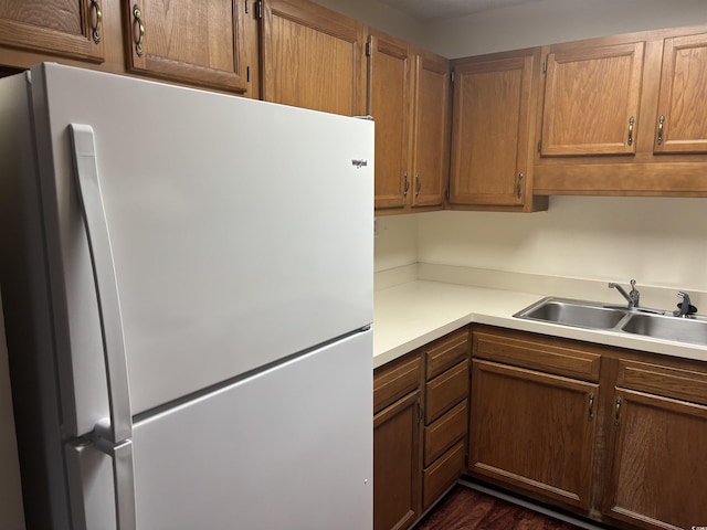 kitchen with dark wood-style floors, light countertops, brown cabinetry, freestanding refrigerator, and a sink