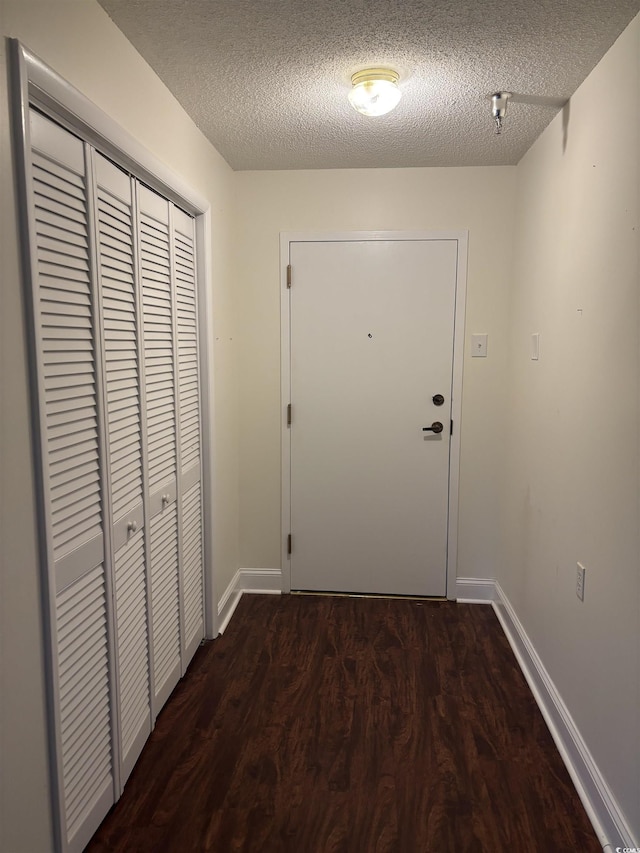 doorway featuring a textured ceiling, dark wood-type flooring, and baseboards