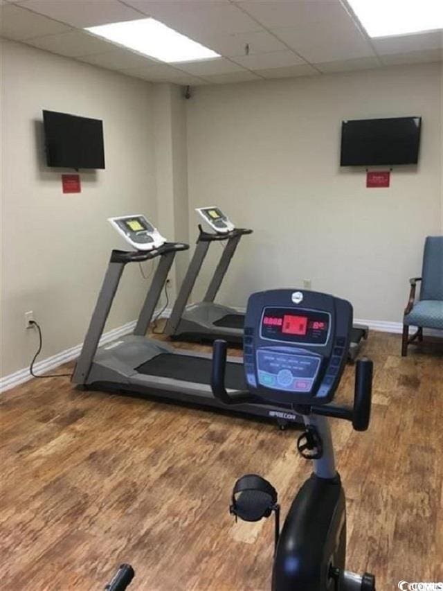 exercise room featuring a drop ceiling, wood finished floors, and baseboards