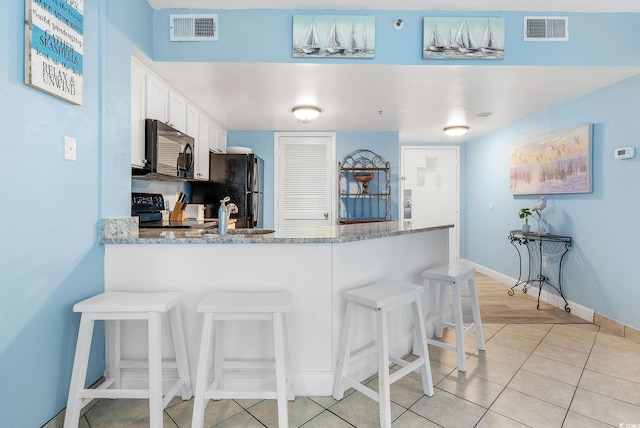 kitchen featuring light stone countertops, a breakfast bar, black appliances, white cabinetry, and light tile patterned flooring