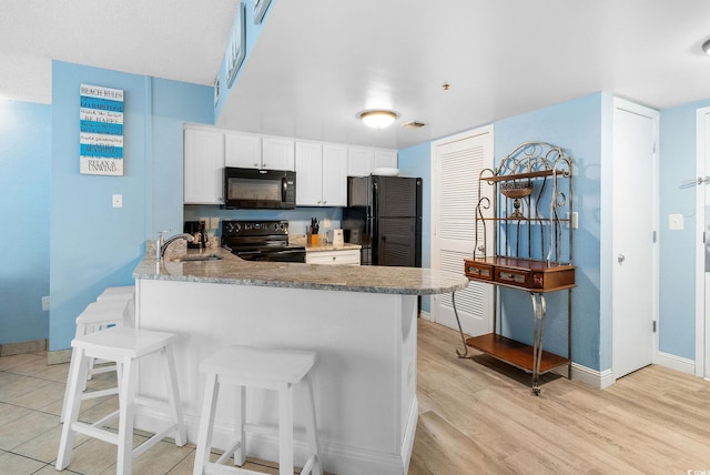 kitchen with kitchen peninsula, sink, black appliances, white cabinetry, and a breakfast bar area