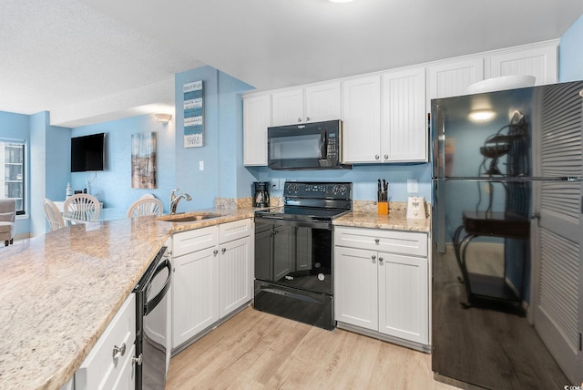 kitchen featuring light stone countertops, white cabinetry, black appliances, and light hardwood / wood-style floors