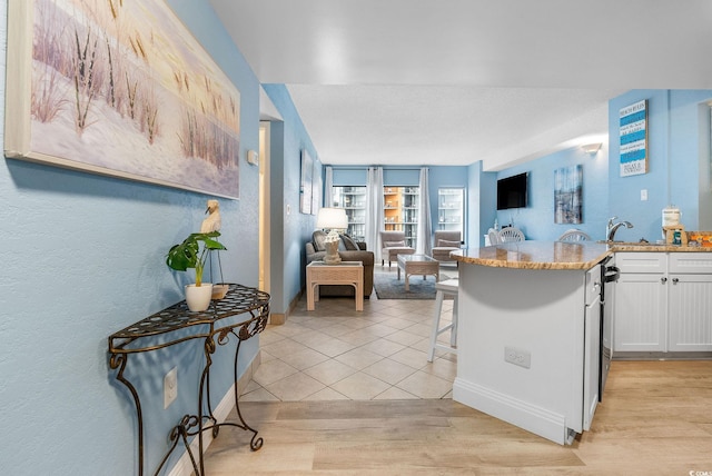 kitchen featuring light stone countertops, sink, light hardwood / wood-style flooring, a breakfast bar, and white cabinets