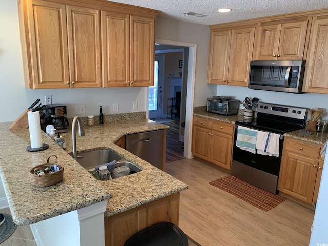 kitchen featuring appliances with stainless steel finishes, light hardwood / wood-style floors, light stone counters, and sink