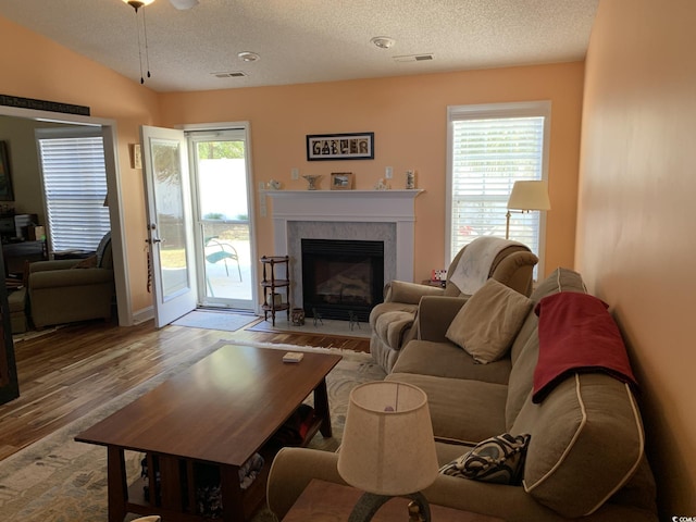 living room featuring a textured ceiling, ceiling fan, light hardwood / wood-style flooring, a fireplace, and lofted ceiling