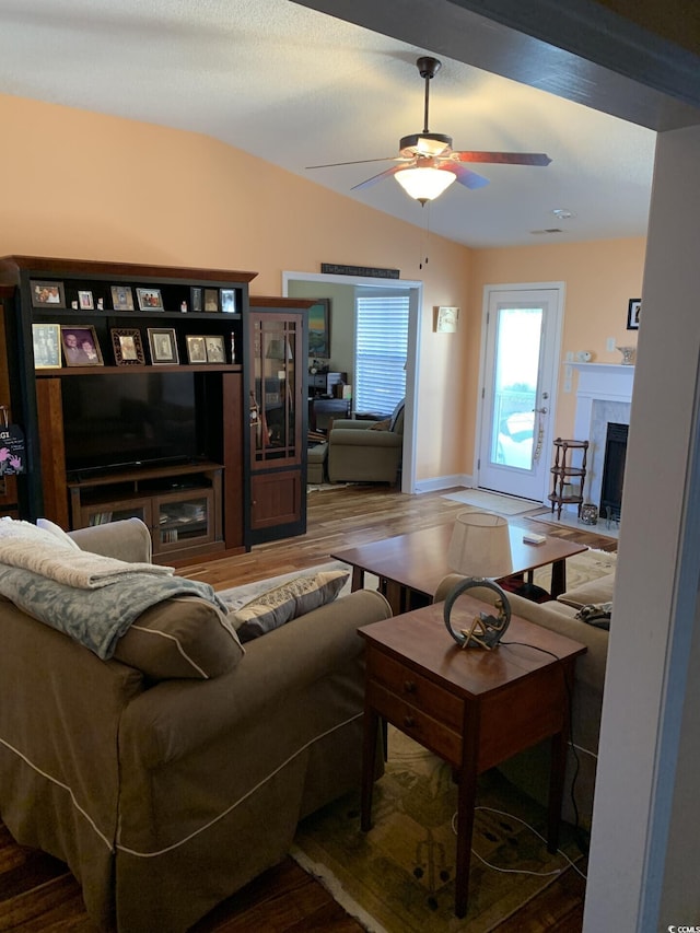 living room featuring a tiled fireplace, ceiling fan, vaulted ceiling, and hardwood / wood-style flooring