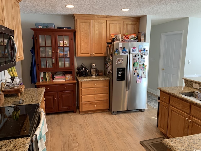 kitchen featuring light stone countertops, a textured ceiling, sink, black appliances, and light hardwood / wood-style floors