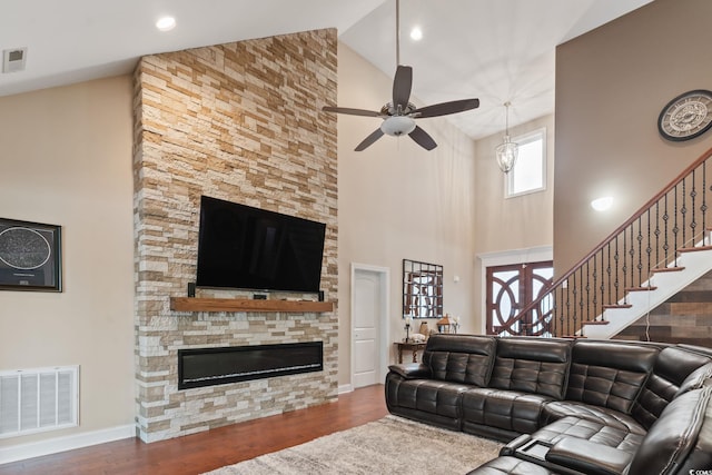 living room featuring dark hardwood / wood-style floors, high vaulted ceiling, and a stone fireplace