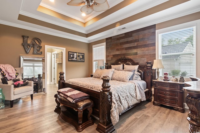 bedroom featuring ceiling fan, light hardwood / wood-style floors, ornamental molding, and a tray ceiling