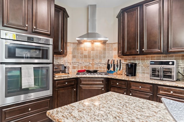 kitchen featuring dark brown cabinets, wall chimney exhaust hood, and appliances with stainless steel finishes