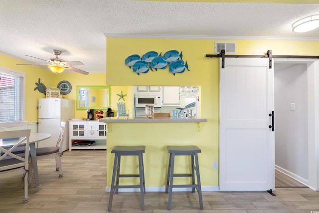 kitchen featuring white appliances, kitchen peninsula, a barn door, crown molding, and a breakfast bar area