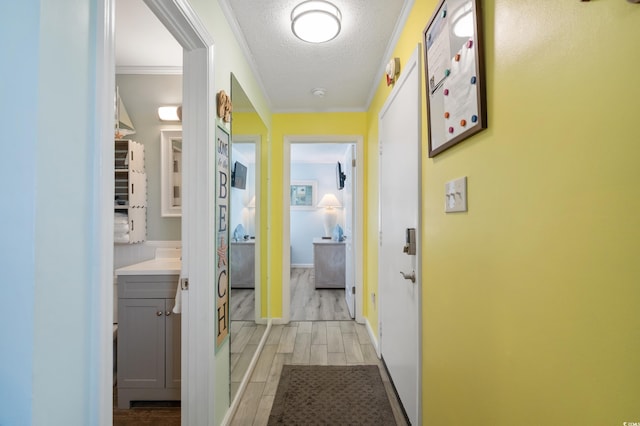 corridor with light hardwood / wood-style floors, ornamental molding, and a textured ceiling