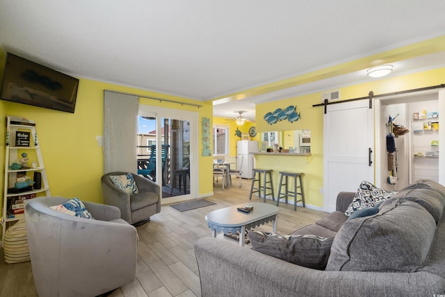 living room featuring ornamental molding, light wood-type flooring, ceiling fan, and a barn door