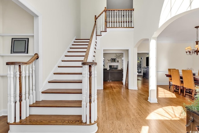 stairs with wood-type flooring, a towering ceiling, and a notable chandelier