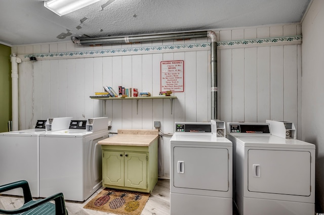 clothes washing area with a textured ceiling, washing machine and dryer, and wood walls