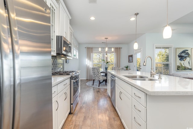 kitchen featuring white cabinetry, sink, pendant lighting, a kitchen island with sink, and appliances with stainless steel finishes