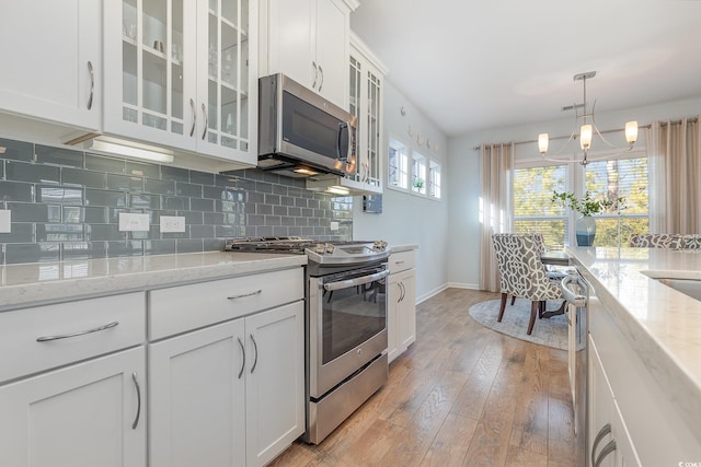 kitchen featuring light stone countertops, tasteful backsplash, stainless steel appliances, a chandelier, and white cabinetry