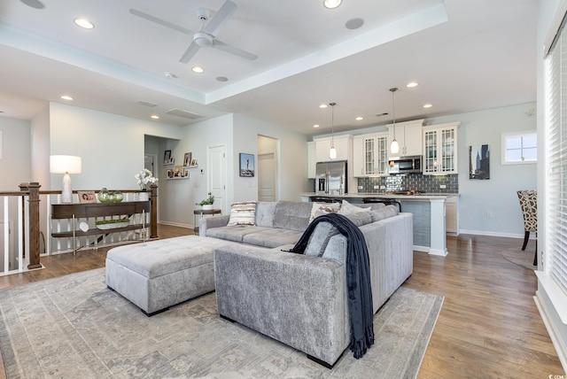 living room featuring ceiling fan, light hardwood / wood-style flooring, and a tray ceiling