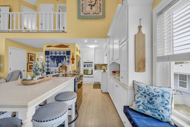 kitchen featuring backsplash, white cabinets, a breakfast bar area, light hardwood / wood-style flooring, and stainless steel appliances