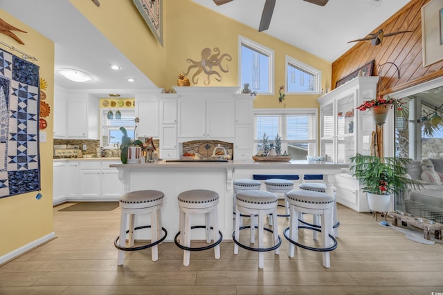 kitchen with backsplash, a breakfast bar, ceiling fan, white cabinets, and light hardwood / wood-style floors