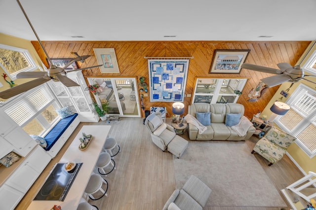 living room featuring ceiling fan, a healthy amount of sunlight, wooden walls, and light hardwood / wood-style flooring