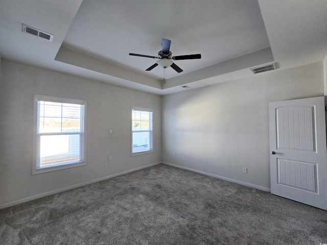 spare room featuring dark colored carpet, a raised ceiling, and ceiling fan