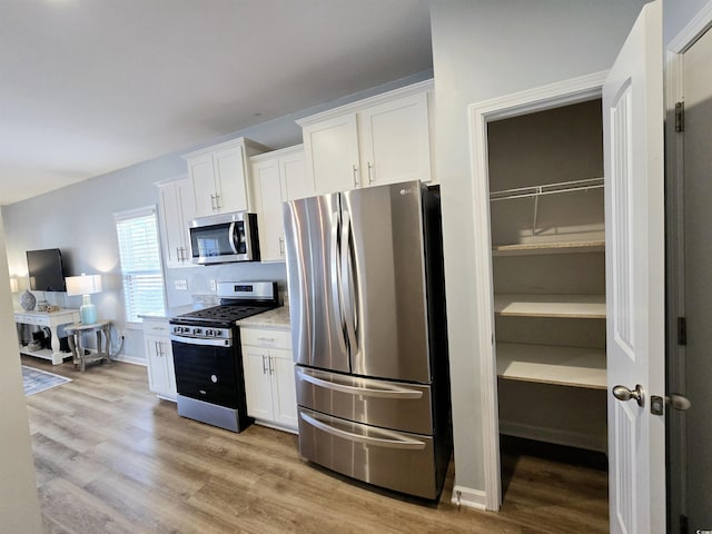 kitchen featuring light stone countertops, appliances with stainless steel finishes, light wood-type flooring, and white cabinetry