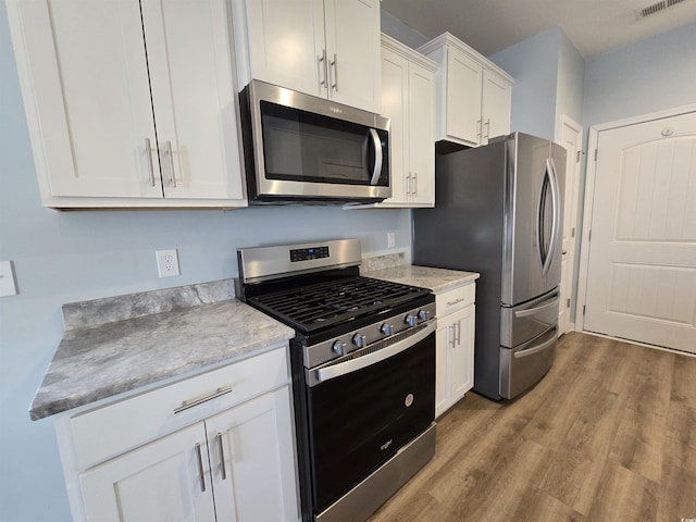 kitchen with stainless steel appliances, white cabinetry, light hardwood / wood-style floors, and light stone counters