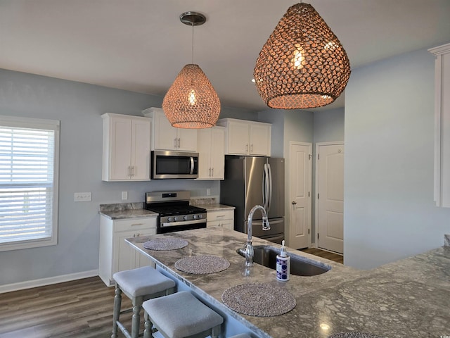 kitchen with white cabinets, a kitchen breakfast bar, hanging light fixtures, sink, and appliances with stainless steel finishes