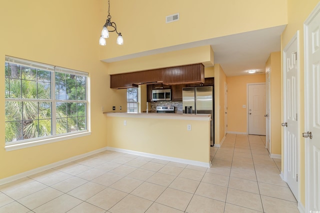 kitchen with stainless steel appliances, decorative light fixtures, light tile patterned floors, and kitchen peninsula