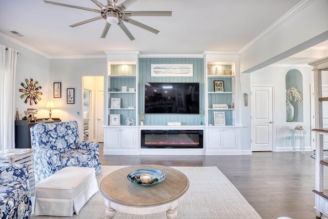 living room featuring built in shelves, dark hardwood / wood-style floors, ceiling fan, and ornamental molding