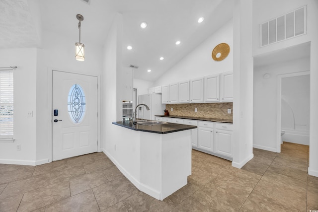 kitchen with kitchen peninsula, sink, pendant lighting, high vaulted ceiling, and white cabinets