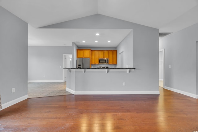 kitchen featuring a breakfast bar, lofted ceiling, dark wood-type flooring, kitchen peninsula, and stainless steel appliances