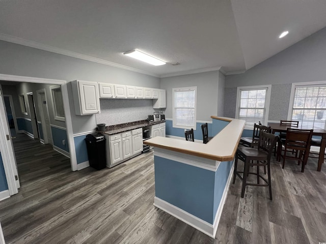 kitchen with a center island with sink, crown molding, a breakfast bar, white cabinetry, and dark hardwood / wood-style floors