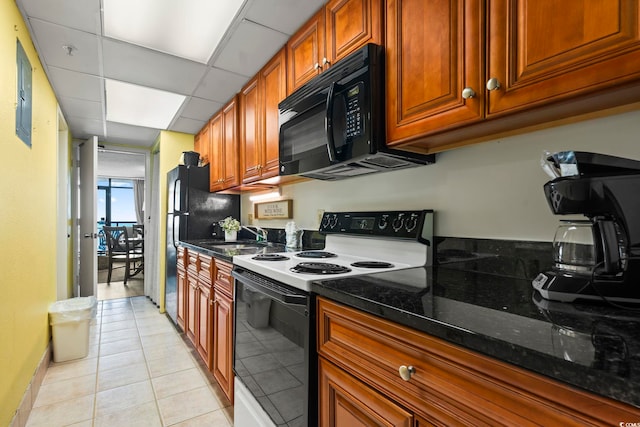 kitchen with dark stone countertops, black appliances, sink, a paneled ceiling, and light tile patterned floors