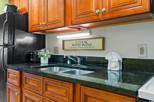 kitchen featuring black fridge, decorative backsplash, dark stone counters, and sink