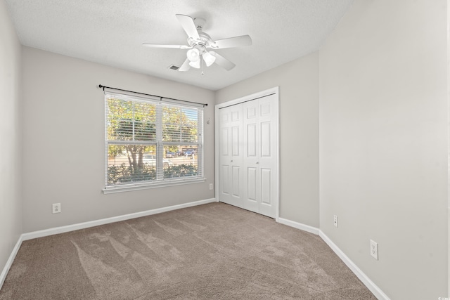 unfurnished bedroom featuring ceiling fan, a closet, light colored carpet, and a textured ceiling