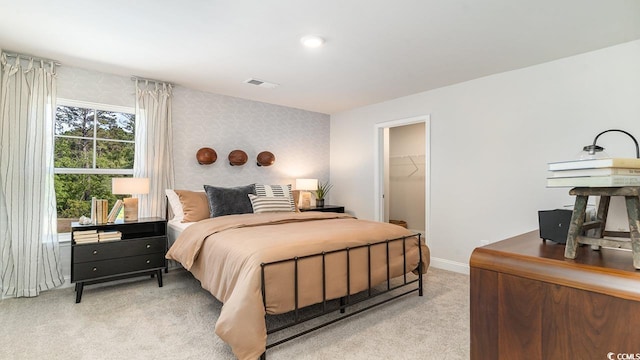 bedroom featuring light colored carpet, baseboards, and a walk in closet