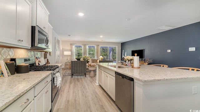 kitchen featuring appliances with stainless steel finishes, a sink, open floor plan, tasteful backsplash, and white cabinetry