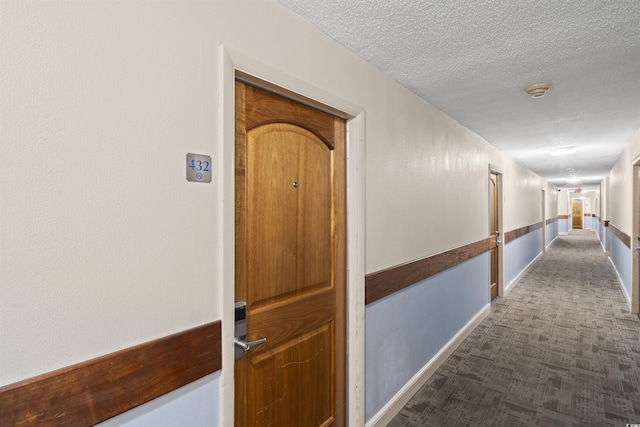 corridor featuring a textured ceiling and dark colored carpet