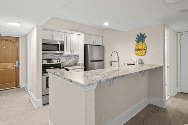 kitchen featuring stainless steel appliances, white cabinets, backsplash, and kitchen peninsula