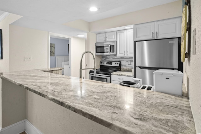 kitchen with stainless steel appliances, white cabinetry, light stone counters, and kitchen peninsula