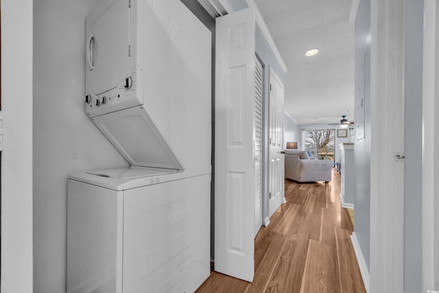 laundry room featuring light hardwood / wood-style floors, stacked washer / dryer, crown molding, and ceiling fan