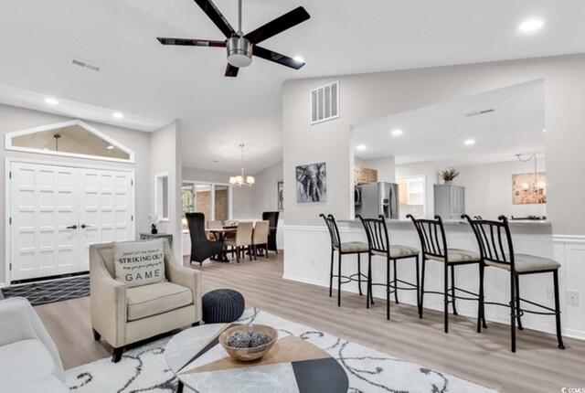 living room featuring ceiling fan with notable chandelier, light hardwood / wood-style floors, and lofted ceiling